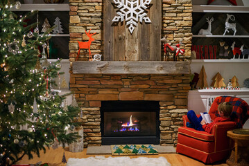 Boy sitting in an armchair by the fireplace reading a book at Christmas