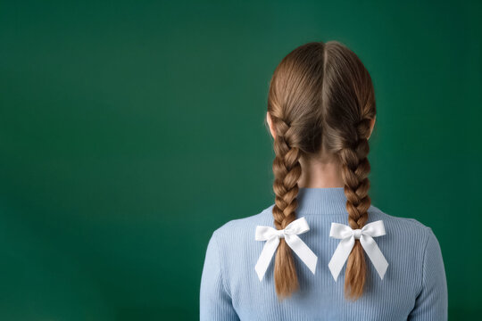 back view of a girl with school braids and bows standing against a green chalkboard background