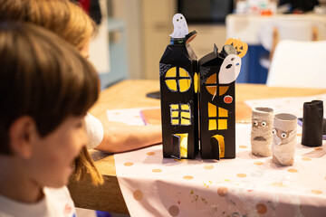 Children looking at black halloween haunted houses made with  upcycled packaging. DIY spooky cheap craft idea.