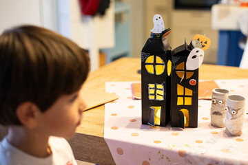 Child looking at black halloween haunted houses made with  upcycled packaging. DIY spooky cheap craft idea.