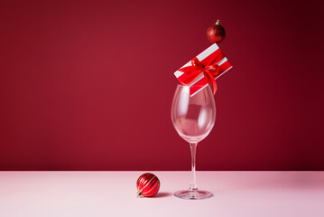 Elegant Christmas still life with wine glasses, red gift box and baubles on red background