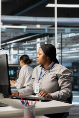 Data center software developer running diagnostic scripts, examining infrastructure. African american server room IT expert using PC to evaluate performance metrics, maintaining system stability