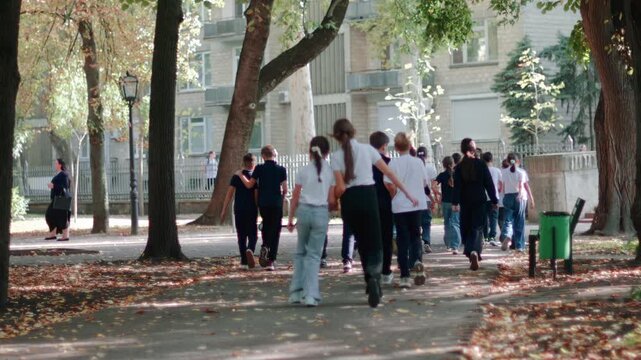 Group of school children strolling under green trees in a sunny park in Chisinau, Moldova