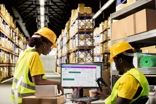 Black industrial employees monitoring parcel status on a computer tracking software, handling e-commerce logistics and shipment route for real time updates. Order fulfillment in depot.