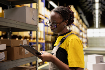 E-commerce depot employee checking parcel details on tablet, processing orders for delivery. Managing cargo inventory and generating shipping labels for large business warehouse activity.