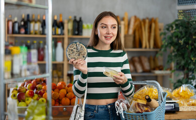 Positive girl with cart in food shop holding and choosing fresh salted herring