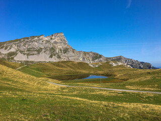 Berglandschaft mit kleinem See unter blauem Himmel. Sanfte H&uuml;gel, steiler Fels und klare Farben in den Alpen &ndash; friedliche Sommerstimmung in unber&uuml;hrter Natur.