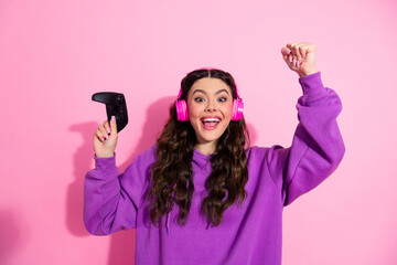 Pretty cheerful woman with gaming controller and headphones excitedly celebrating her achievement...