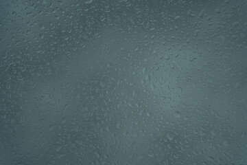 Raindrops on a grey surface creating a textured and abstract pattern.