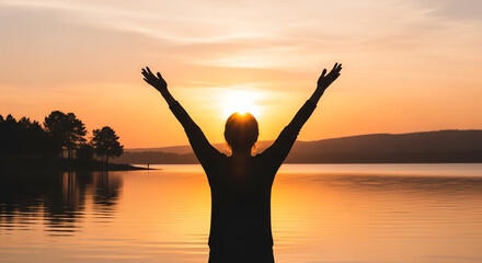 Silhouette of a man with raised arms from behind, looking at the sunset.