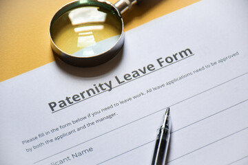 Close-up of a paternity leave form with magnifying glass on table. Paid leave or extension of paternity leave concept. Selective focus.