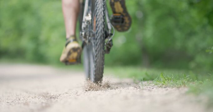 Abstract mountainbiker getting ready to ride. Throwing pebbles. Man riding a mountainbike on a dusty dirth road path. Closeup pedal shoe and gear shift. Recorded at 120 fps on cinema camera.
