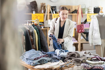 Positive young woman choosing jeans trousers during sell-out season in clothing shop