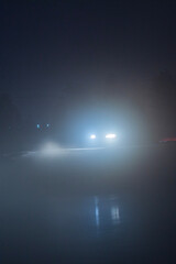 a car with fog lights on at night, when driving is impossible and dangerous with poor visibility, against the background of the night sky and slippery roads in winter on ice