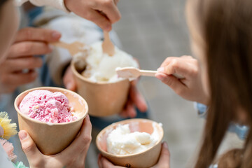 Closeup of children enjoying different flavors of ice cream holding paper cups with spoons. The scene captures the joy of summer treats and shared moments