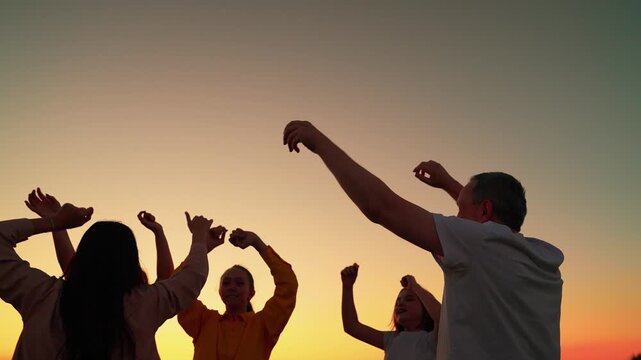 Party dancing, group of happy people raising their hands to sky in evening. People having fun outdoors, dancing on beach, relaxing in nature. People dancing to music concert, raising their hands up.