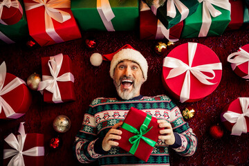 Joyful elderly man in festive sweater holding Christmas gifts surrounded by vibrant decorations and...