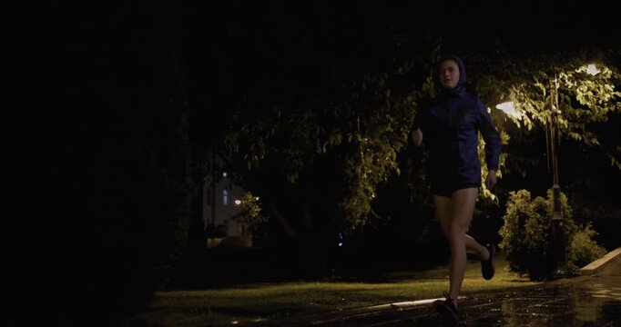 Dedicated runner braving the night storm, jogging with determination along a wet, dimly lit path. Resilience and fitness meet in an inspiring display of persistence and commitment.