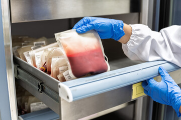 Close up scientist hand wear blue gloves holding red blood bag in storage refrigerator at blood bank unit laboratory.Blood bags received from blood donations used in patients.Save life medical concept