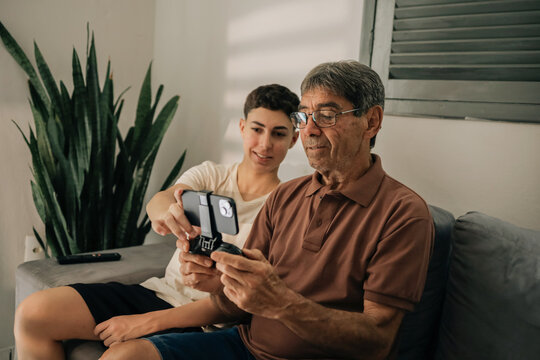 Teenager teaching his grandfather how to play mobile game using smartphone controller at home