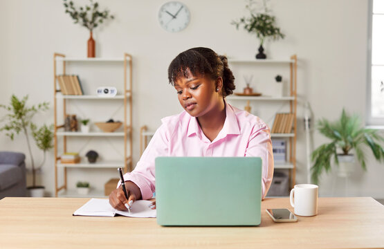 Middle aged african american woman working with laptop at home, housewife planning, uses internet, searching information, writing, enjoy weekend at distant learning, ordering goods or food on-line - Powered by Adobe