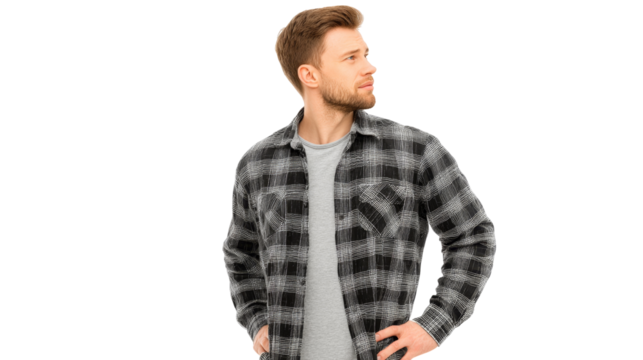 Young man with beard, wearing plaid flannel shirt and t-shirt, stands casually with hand on hip, looking to the side.
