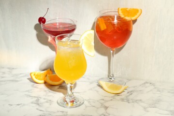 Glasses of tasty cocktails with garnish on white marble table
