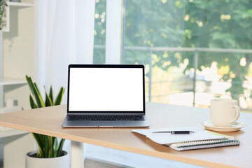 Fototapeta premium Laptop with empty white screen and stationery on desk in room. Comfortable home workplace
