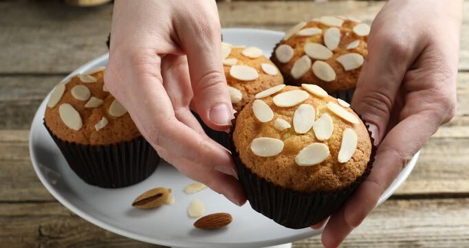Woman taking tasty muffin with almond flakes at wooden table, closeup