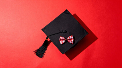 Graduation cap with tassel and decorative bow on red background in a top-down view composition. event programs, museum guides, designed for cultural heritage projects and event programs.
