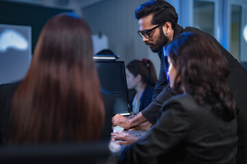 A diverse and dedicated team of professionals works diligently in a bustling, modern tech office at night, collaborating and focusing on their tasks to meet a critical project deadline.