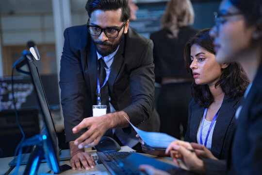 A senior data scientist with glasses points out an anomaly in a machine learning model's code to two female AI engineers, as they finalize the algorithm for a new predictive analytics service.