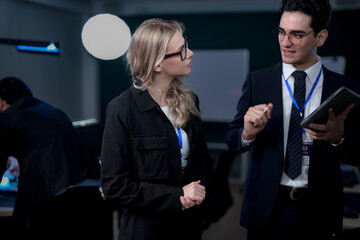 A male team leader in a suit uses a stylus to explain a complex project on a large screen, providing one-on-one training to a female colleague in a modern, high-tech office.