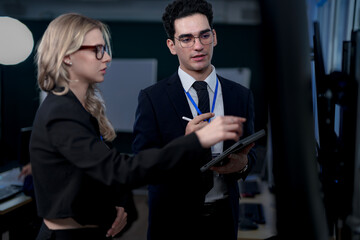 A senior software developer leads a code review session, pointing to a specific function on the screen to explain its logic and syntax to a junior engineer before a major deployment.