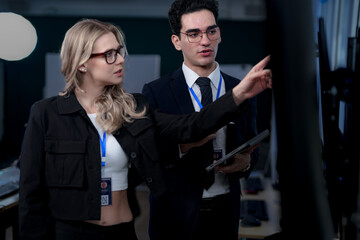 A male team leader in a suit uses a stylus to explain a complex project on a large screen, providing one-on-one training to a female colleague in a modern, high-tech office.