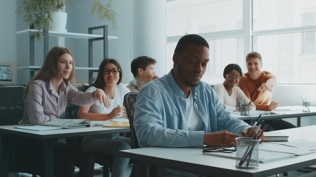 In a bright and inviting classroom, a group of diverse college students bullying lonely African American guy