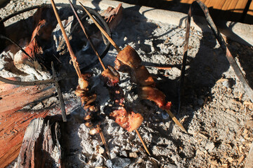 Grill pork on traditional open fire stove glowing wood burning under morning sunlight. Camping Traditional outdoor cooking.