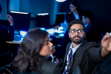 A diverse team of professionals collaborates on a business strategy late at night. A male manager uses a tablet and stylus to explain key points to his female colleague in a modern boardroom.