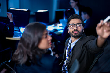 A diverse team of professionals collaborates on a business strategy late at night. A male manager uses a tablet and stylus to explain key points to his female colleague in a modern boardroom.