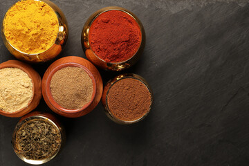 Overhead top view flat lay colourful array of spices herbs powder blue clay ceramic brass metal pot on dark black slate surface with a clean and neat appearance spice copy text space border frame