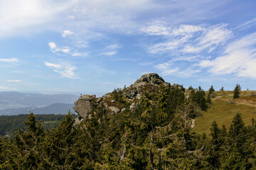 Wide view from the Arber summit in the Bavarian Forest with rocky formations, evergreen trees and a bright blue summer sky.