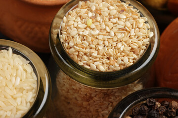 Top down flat lay view of white sesame seeds in mini glass jar on dark black slate background