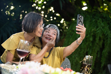 Senior women selfie outdoor garden, happy friends sharing activities and learning with technology over wine, candid smile, summer light, greenery background, warm joy, close bond