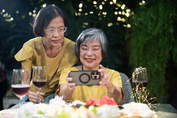 Senior women friendship garden dinner selfie smartphone candid smile warm light social joy