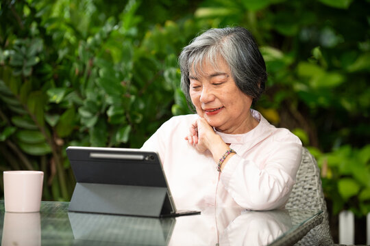 Senior woman tablet garden leisure retirement learning technology activities friends smile gray hair outdoor natural light relaxed lifestyle connection - Powered by Adobe