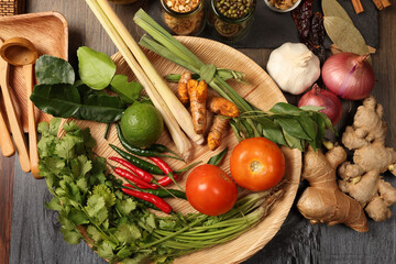 colourful fresh vegetables and herbs turmeric lemon grass lime leaf tomato red green chilli coriander on palm leaf plate wooden board for healthy cooking meals