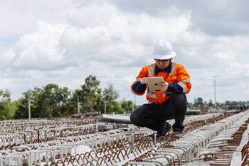 Construction engineer inspecting reinforcement steel bars at a bridge construction site using a digital tablet.