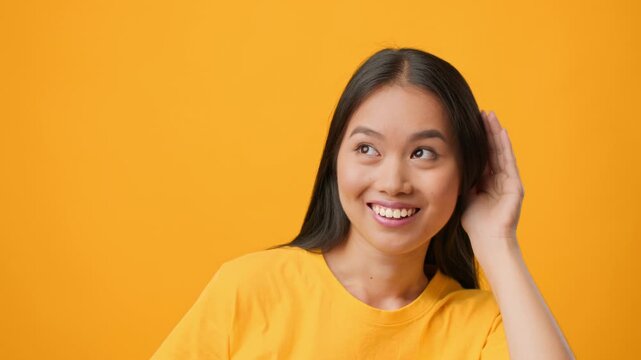 A young Asian woman with long hair demonstrates a playful attitude while wearing a bright yellow shirt. Her expression captures a mix of sass and humor against a vivid yellow backdrop.