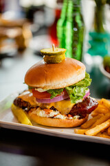 A hot chicken sandwich covered in sauce with cheese tomato lettuce onion and coleslaw in a bright restaurant 