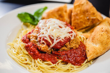 Chicken Parmesan dish on a white plate with a garnish and homemade bread 